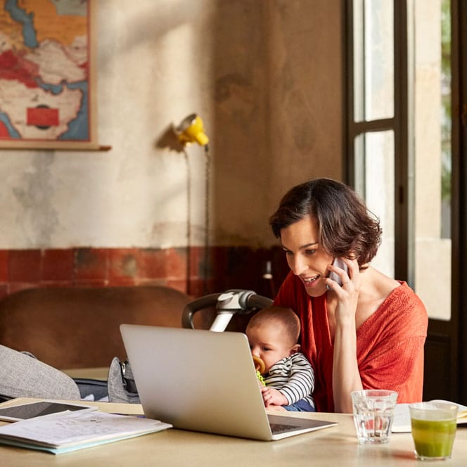 Adult on the phone while holding a child and looking at a laptop