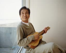 Senior man sitting by window playing ukelele, looking up