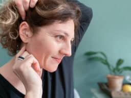 Woman adjusts hearing aids behind ear