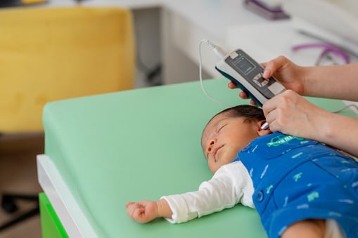 Doctor performing hearing test on sleeping newborn baby girl in a medical office.