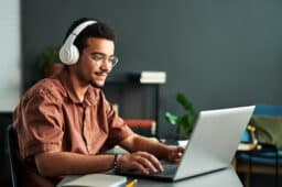Young man wearing headphones, siting at his laptop.