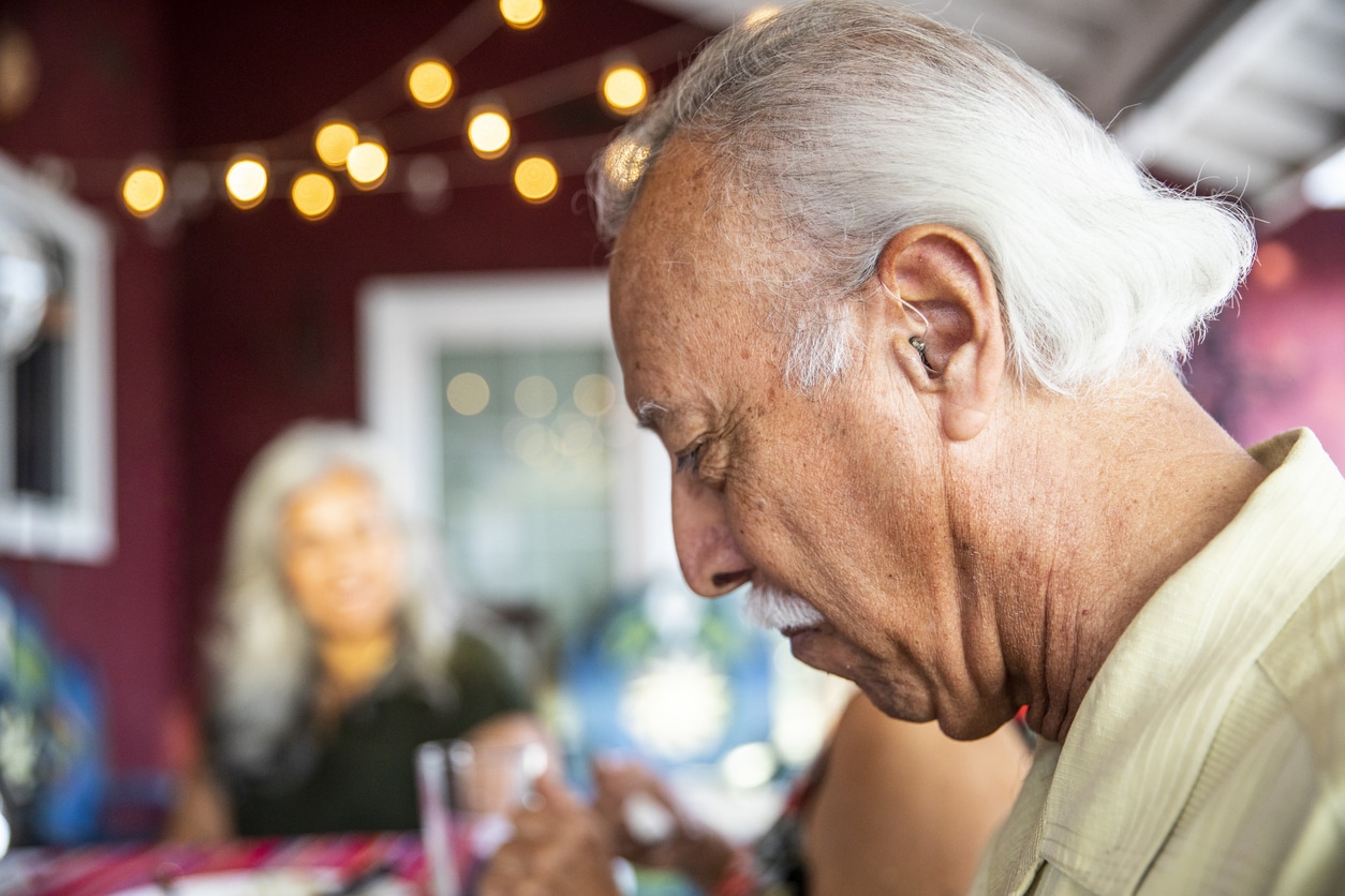 Senior man wearing his hearing aid at a restaurant.