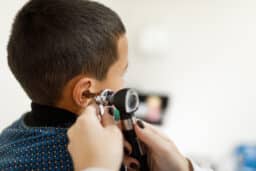Doctor looking at a young boy's ear with an otoscope.