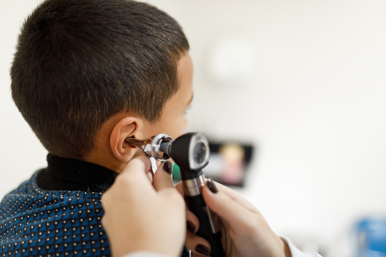 Doctor looking at a young boy's ear with an otoscope.