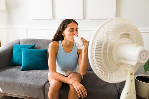Woman trying to cool off in the summer with a fan and glass of ice water.