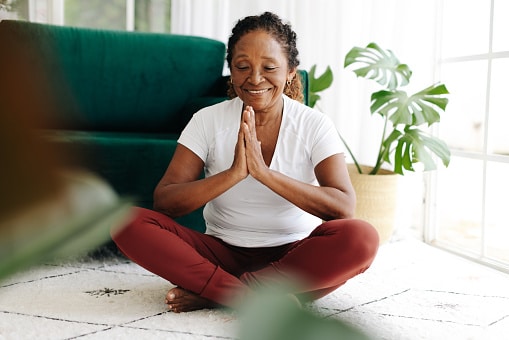 Senior woman improving mental wellbeing through yoga, meditating at home with a serene smile.